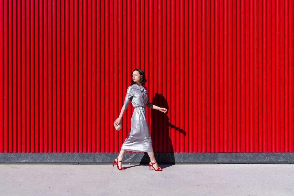 Žena v dlouhých stříbrných šatech a červených sandálech na podpatku na červeném pozadí