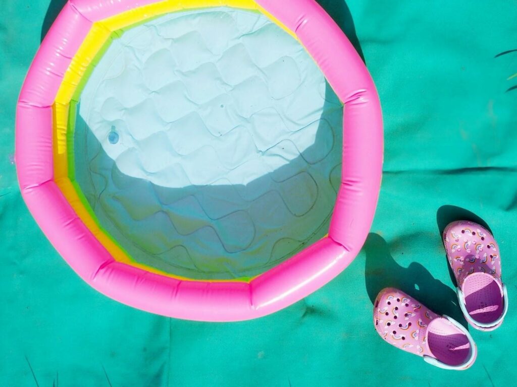 Růžové dětské boty Crocs vedle malého barevného bazénu