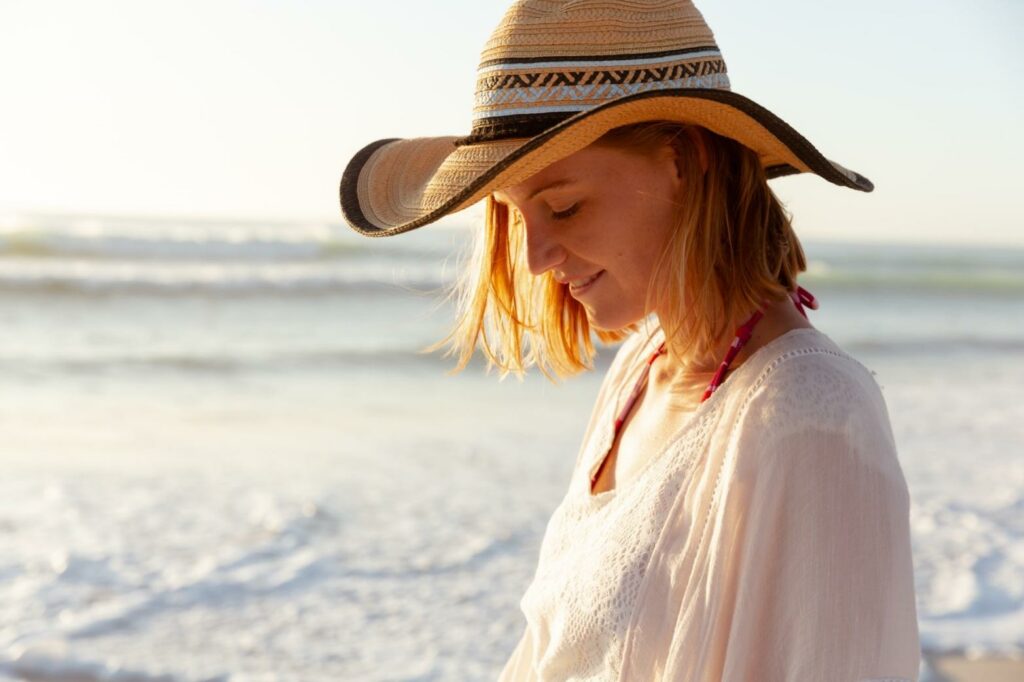 Na pozadí moře stojí žena v klobouku a bílé halence