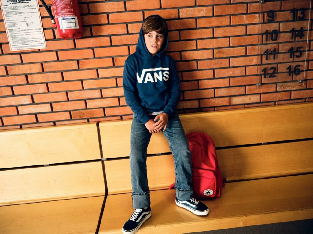 chlapec v mikině, plátěnkách značky Vans a batohem značky Converse