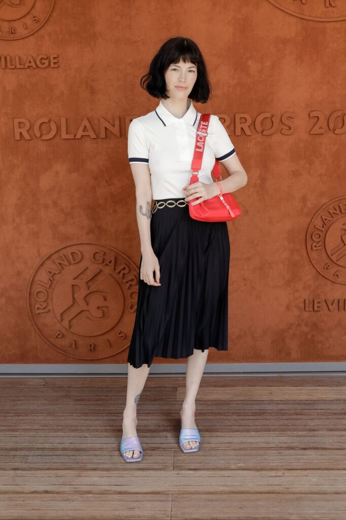 Stojící žena v černé sukni do kolen a bílé polokošili s červenou kabelkou na rameni