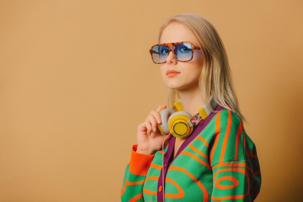 Mladá žena v barevném svetru a brýlích. Sluchátka zavěšená na krku