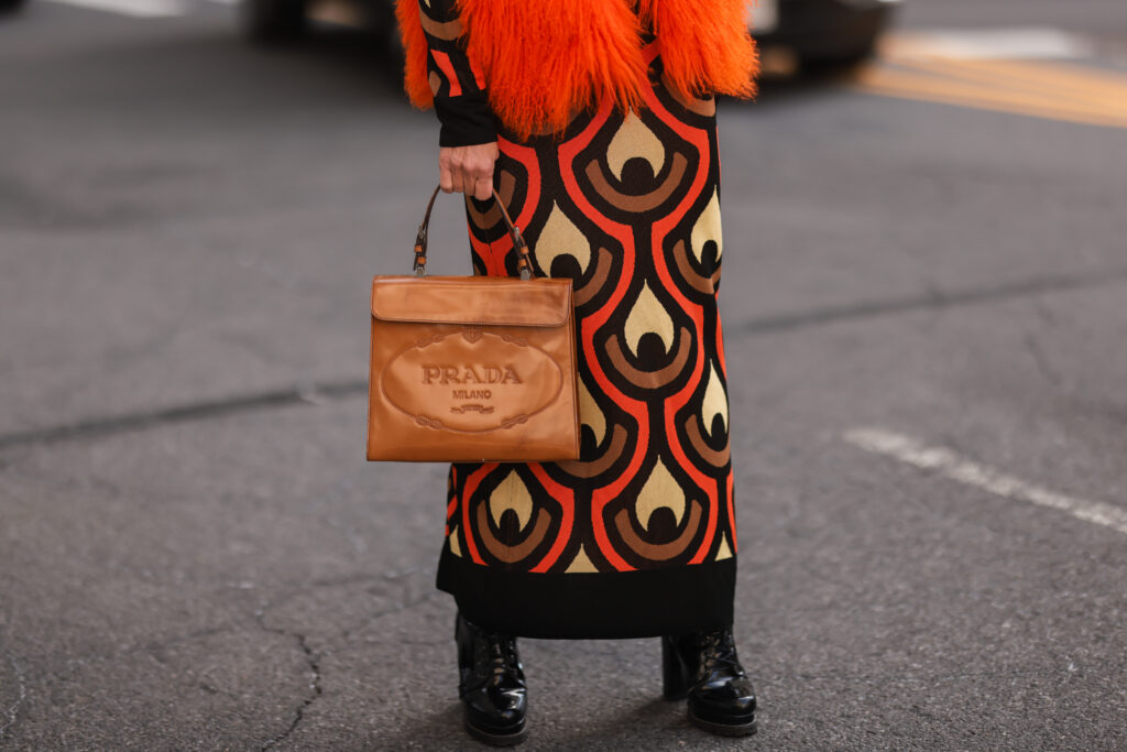 žena v úpletových šatech s hnědou kabelkou Prada