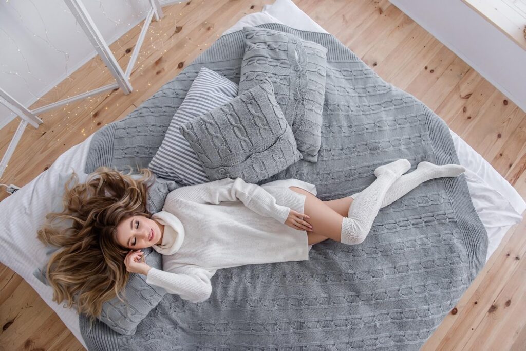 Mladá žena v bílých úpletových šatech s rolákem ležící na matraci