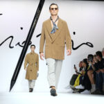 Pánská móda: trendy jaro/léto 2024 na přehlídkových molech – model v kabátu ve velbloudí hnědé a šátkem na krku