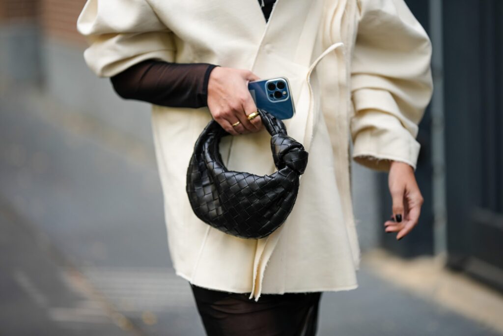 malá černá kabelka držená v ruce, bílý kabát