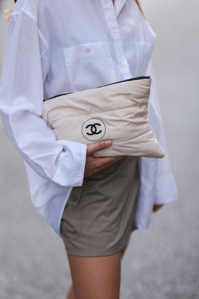 bílá kabelka držená v ruce, bílá košile, hnědé kraťasy