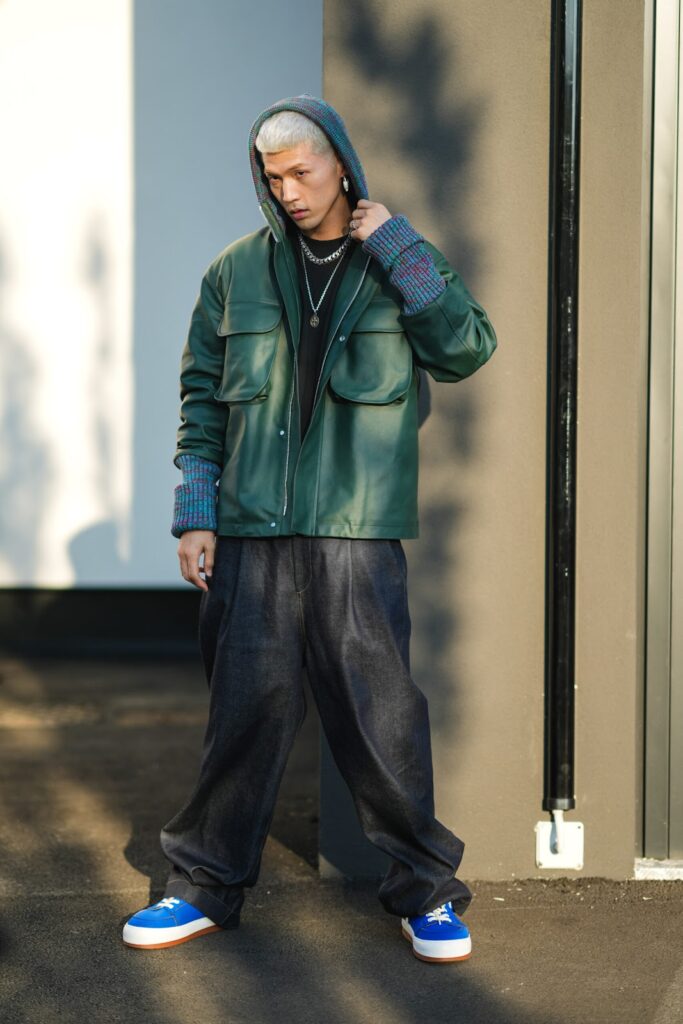 Muž, který má na sobě zelenou bundu s kapucí. Na nohou má obuté modré tenisky.