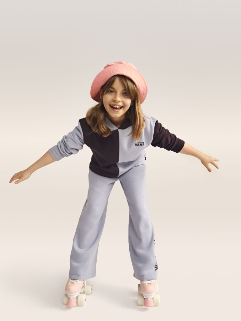 Bruslící dívka v klobouku v teplákové soupravě Vans.

