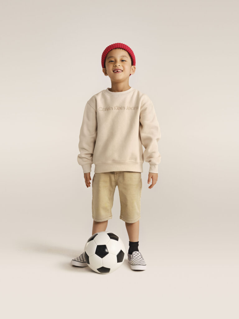 Chlapec v teniskách Vans v béžové mikině Calvin Klein Jeans.
