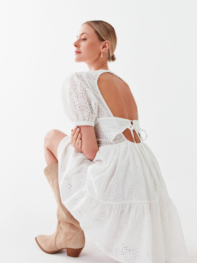 Modelka v bílých ažurových letních šatech s odhalenými zády
